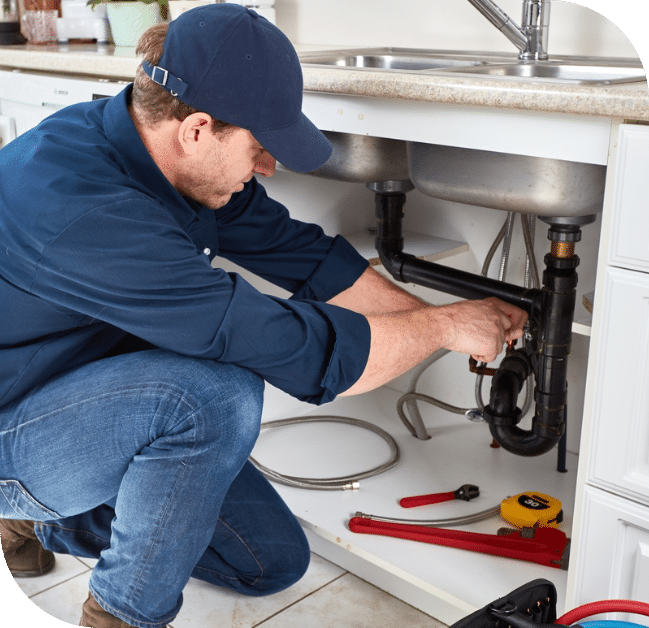 Plumber repairing a pipe under a kitchen sink with tools nearby