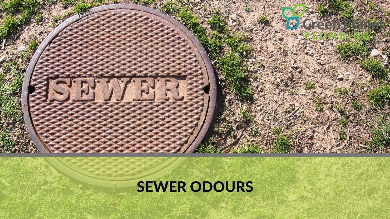 A circular sewer manhole cover with the word "SEWER" embossed on it, surrounded by dry grass and dirt.